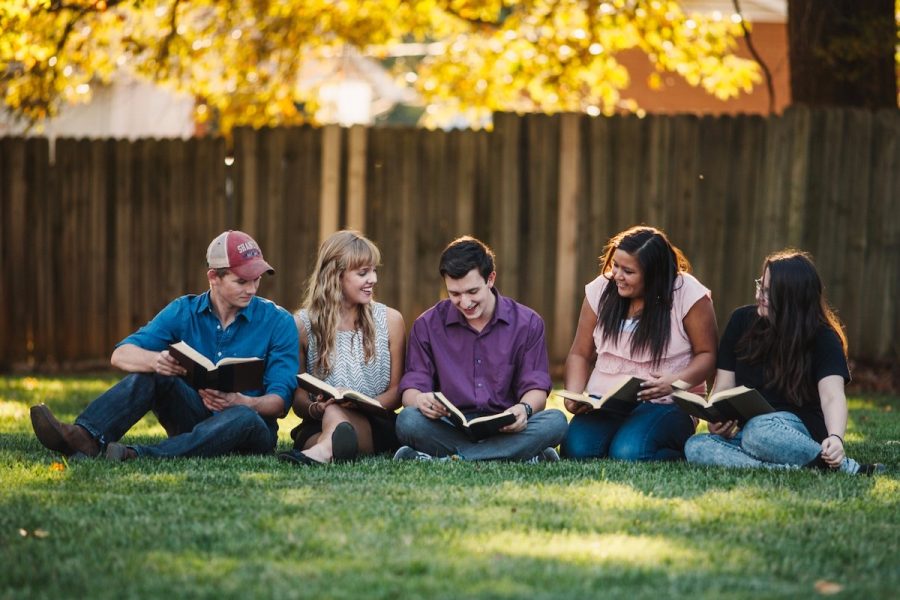 high school age students read and discuss books on a grassy backyard lawn during the afternoon